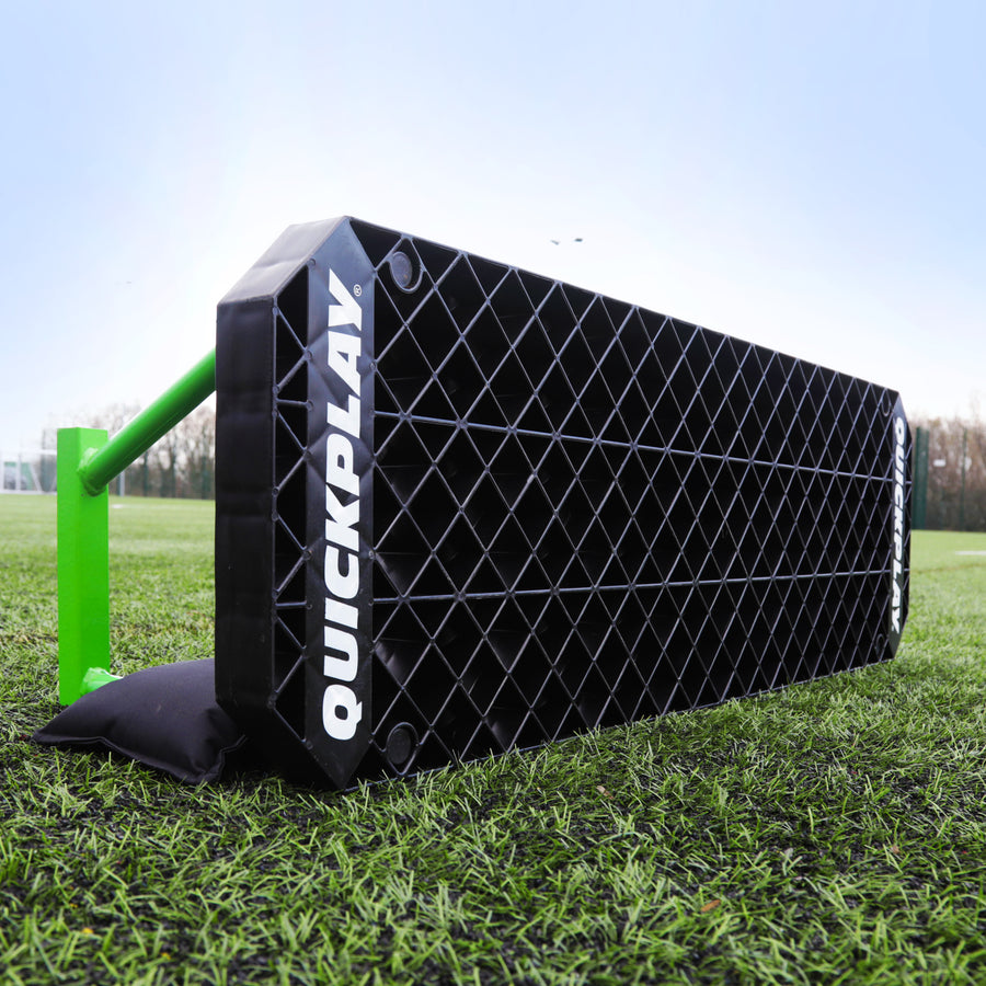 REPLAY Station XL rebound board on artificial grass, low side view showing its black grid face, green frame and black bag.