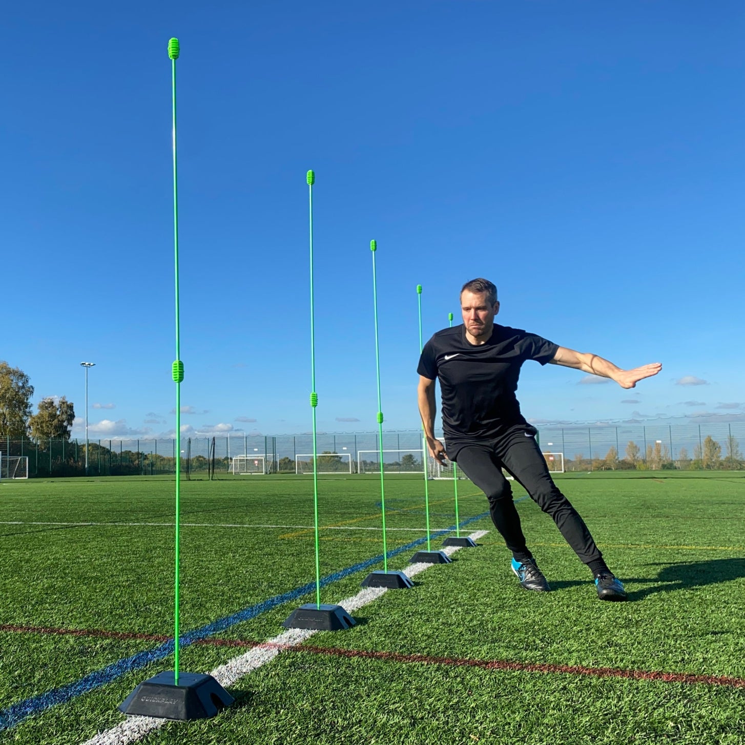 Base Weight set of 2 for KICKSTER, SPOT and agility poles: player stepping through a line of green poles set in black base weights on a pitch.