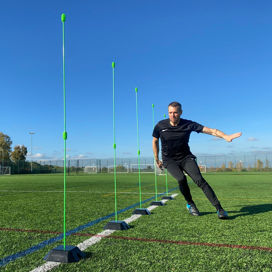 Base Weight set of 2 for KICKSTER, SPOT and agility poles: player stepping through a line of green poles set in black base weights on a pitch.