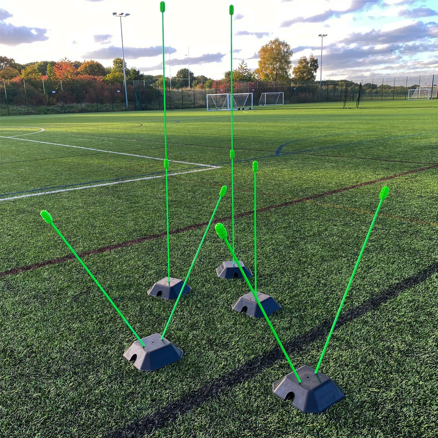 Base Weight set of 2 for KICKSTER, SPOT and agility poles: black base weights with green poles set up at different heights on an artificial pitch.