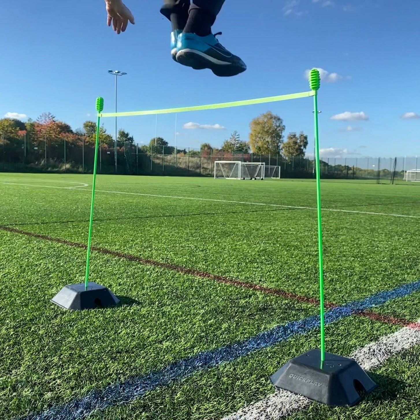 Base Weight set of 2 for KICKSTER, SPOT and agility poles: two base weights hold green poles and a crossbar as a hurdle while a player jumps over.