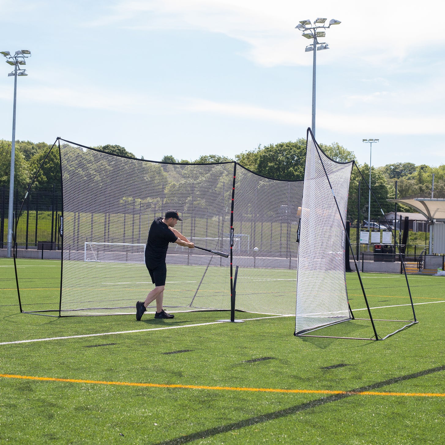 Man hitting a ball with a baseball bat into two MEGA NETs joined by the Extender Net 240 x 270 cm, a black bag at his feet.