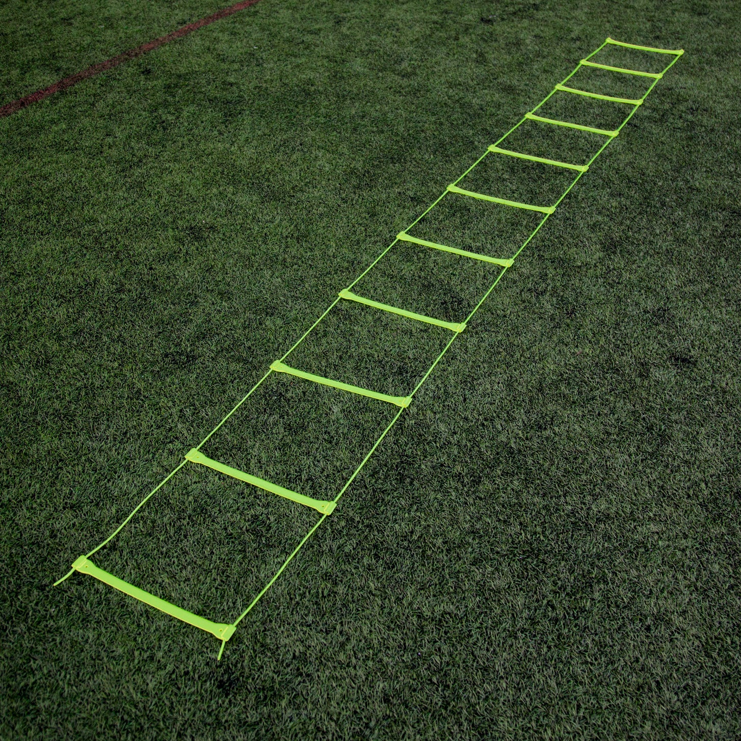 Yellow Agility Ladder laid out flat at full length on an artificial pitch, seen from one end.