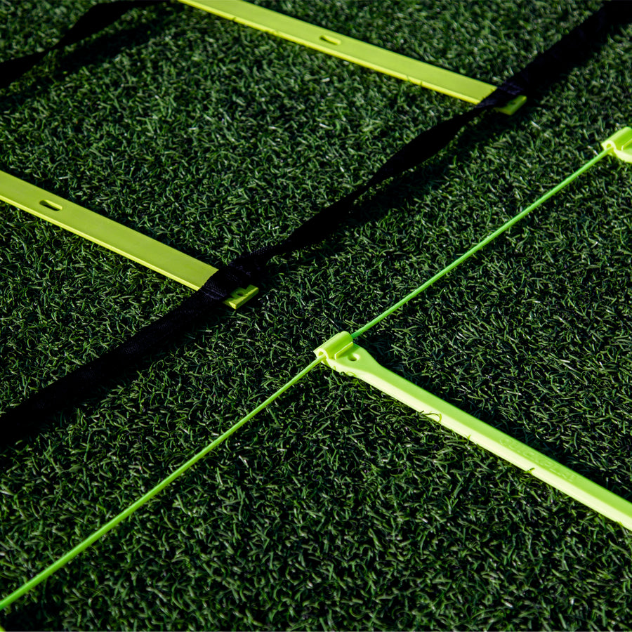 Close-up of yellow Agility Ladder rungs on artificial grass, one ladder with black straps and one with a thin green cord.