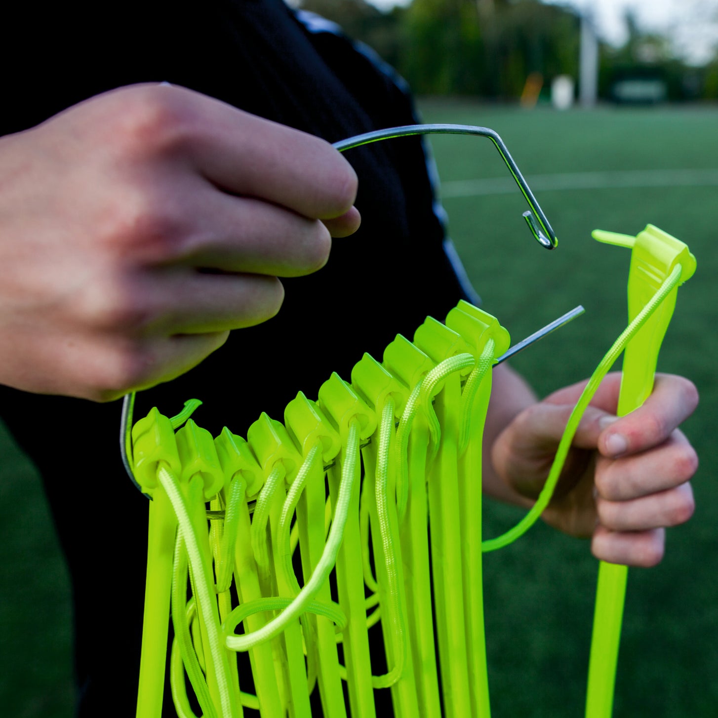 Close-up of hands sliding yellow Agility Ladder rungs onto a metal hook for storage.