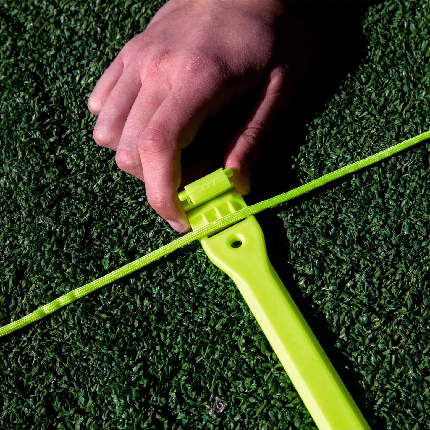 Close-up of a hand clipping the Agility Ladder cord into a yellow rung on artificial grass.