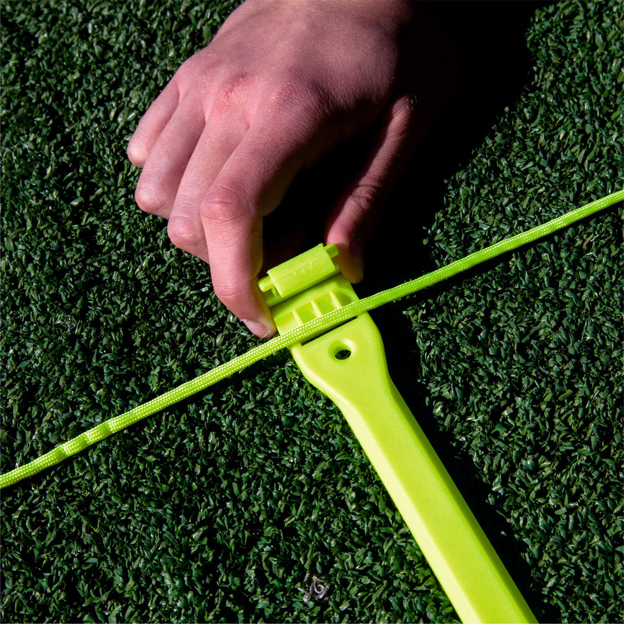 Close-up of a hand clipping the Agility Ladder cord into a yellow rung on artificial grass.