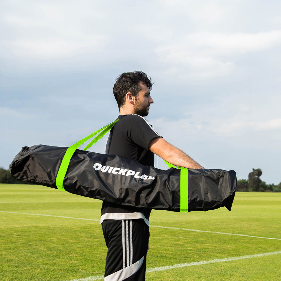 Man carrying the MEGA NET 370 x 270 cm in its black QUICKPLAY bag with green straps on a grass field.