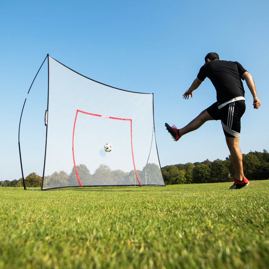 Player kicking a ball into the MEGA NET 370 x 270 cm on grass, the ball heading for the orange target frame.