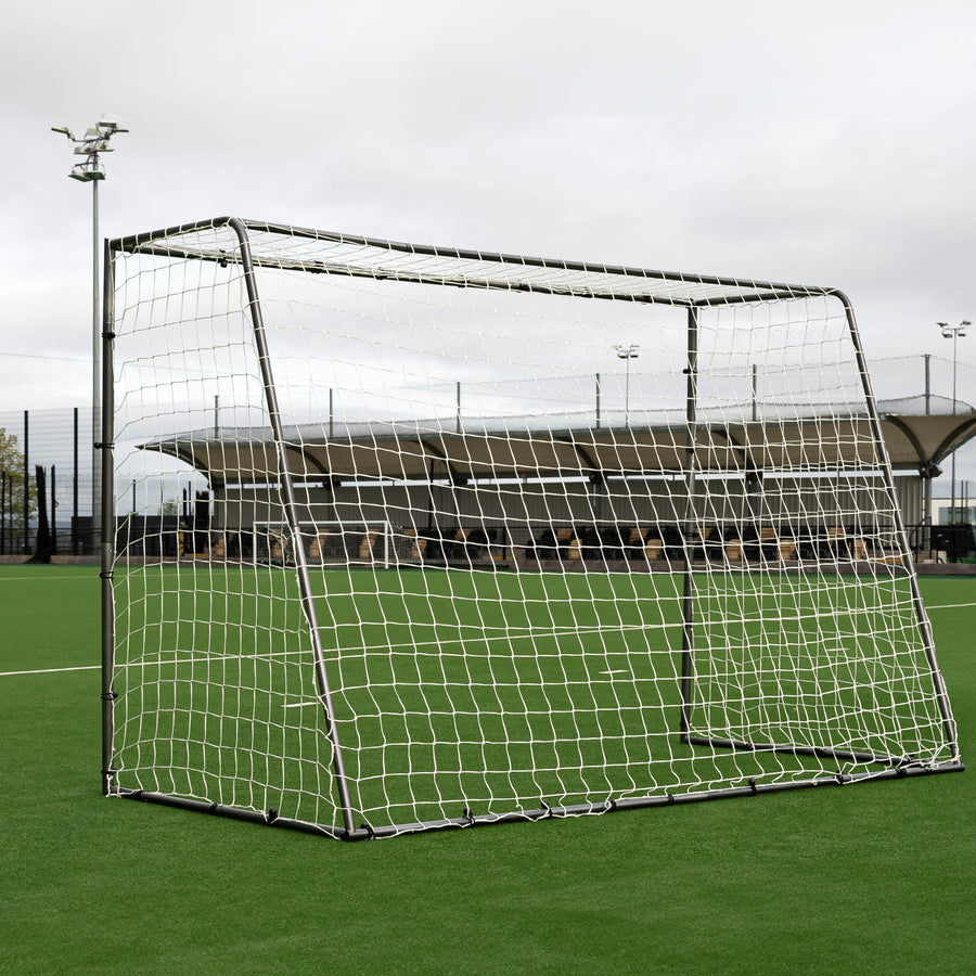 GS Series Futsal Goal 300 x 200 cm from a low angle on an artificial pitch, under a cloudy sky with floodlights behind.