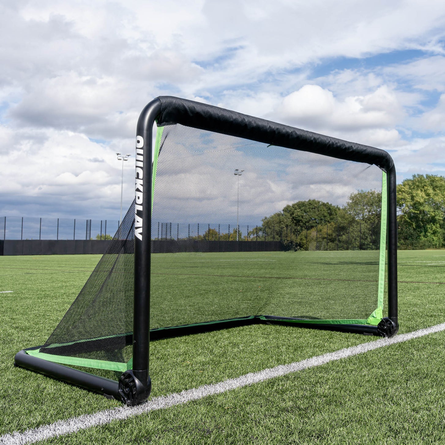 RHINO Football Goal 150 x 100 cm set up on an artificial pitch under a cloudy sky, with trees beyond the fence.