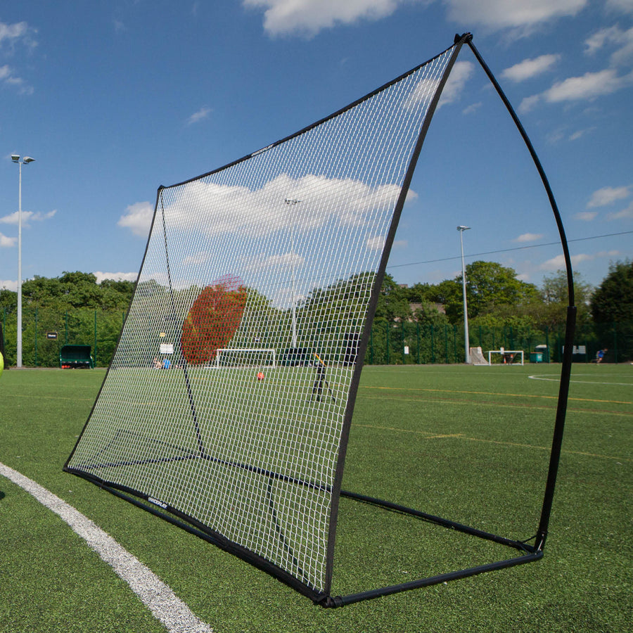 SPOT Football Rebounder 210 x 210 cm on an artificial pitch, angled net with a red target area, seen from the side.