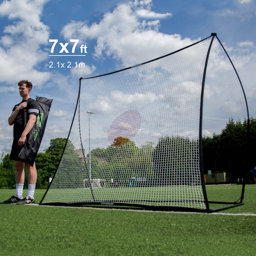 SPOT Football Rebounder 210 x 210 cm on a pitch next to a player holding its bag, with text 7x7 ft, 2.1 x 2.1 m.