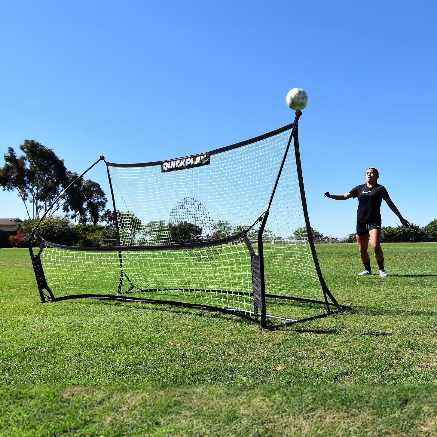 Player waiting for a ball bouncing up off the TEKKERS Trainer Dual Net Football Rebounder on a grass field.