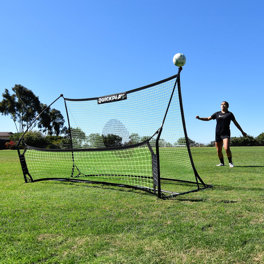 Player waiting for a ball bouncing up off the TEKKERS Trainer Dual Net Football Rebounder on a grass field.