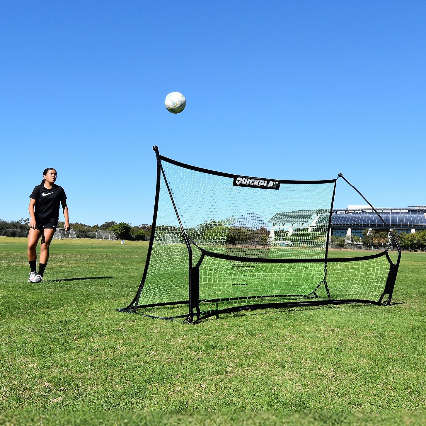 Player watching a ball rise off the TEKKERS Trainer net, front view of the rebounder on a grass field.