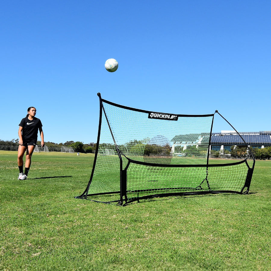 Player watching a ball rise off the TEKKERS Trainer net, front view of the rebounder on a grass field.